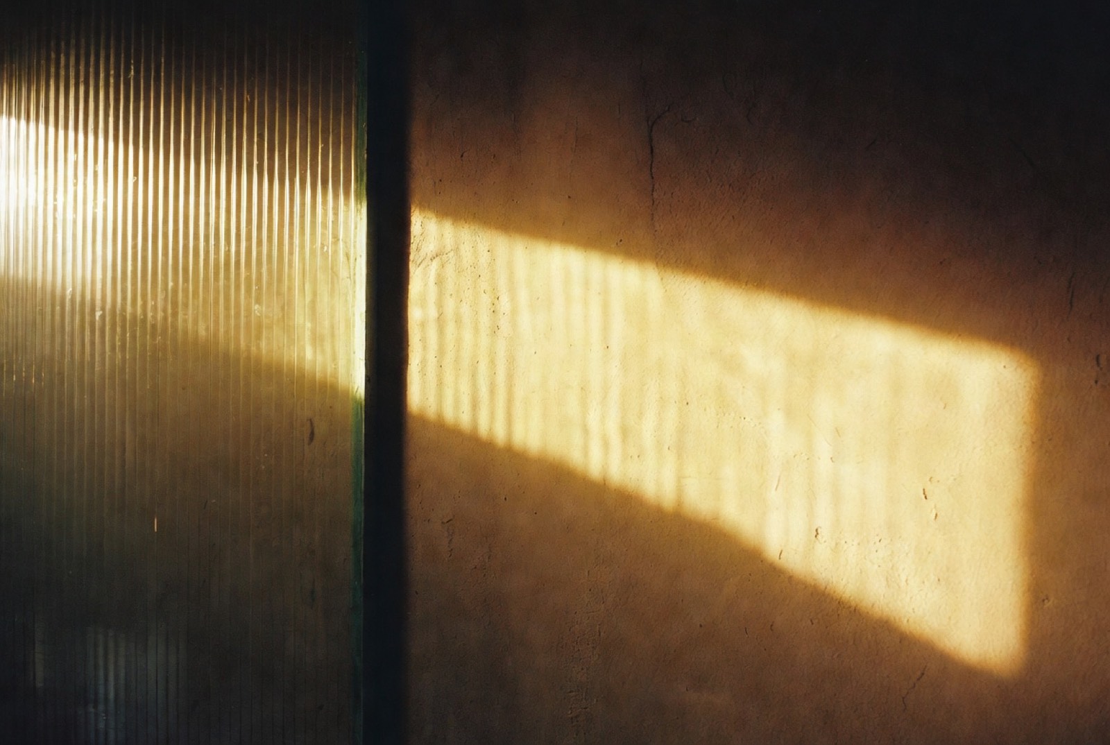 Dawn light through fluted glass, split into bands on a plaster wall